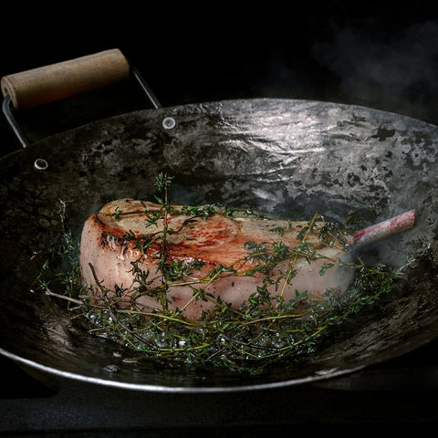 Handgeschmiedete Wok-Pfanne mit Steak und frischen Kräutern, ideal zum Kochen für Gourmets.