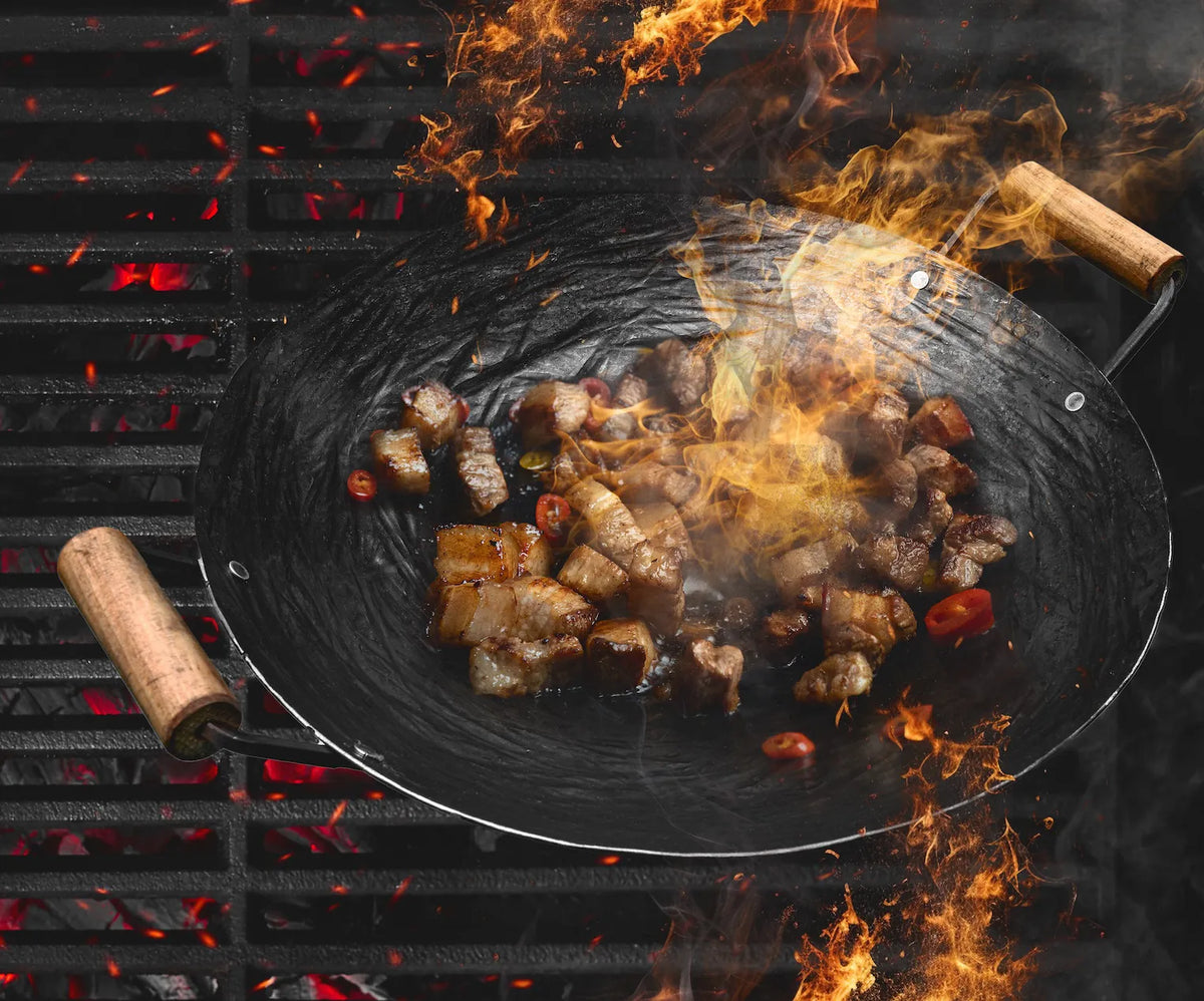 Handgeschmiedeter Wok über Flammen auf dem Grill